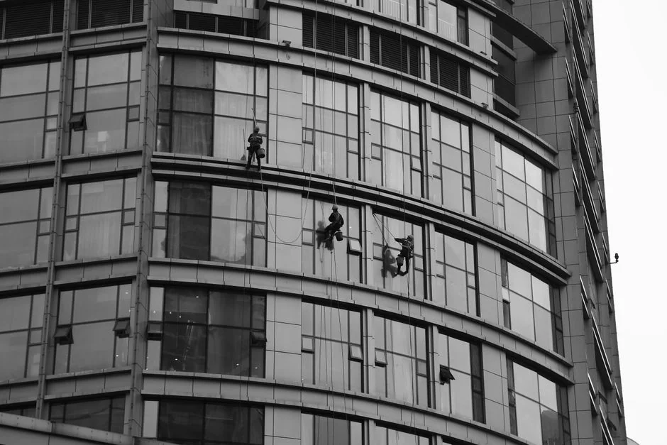 A man is cleaning a glass window with a mop in grayscale, highlighting professional workmanship.
